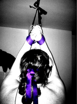 Woman tied to ceiling hook with purple blindfold