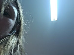 Half face of woman looking down at the viewer with ceiling light behind her head