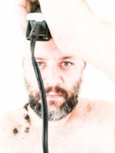 Man with piecring blue eyes shaving his head with clippers