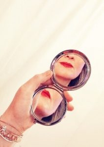 Woman holding companct mirror with reflection of her red lips showing in the mirror