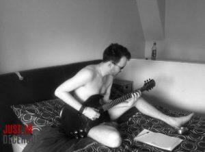Nude man playing guitar on bed