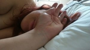 Woman laying in bed covering her face with her hand, grinning