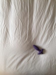 Butt plug left on bed with crumpled sheet as backgroun