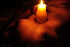 Nude woman with wax on her breasts holding lit candle