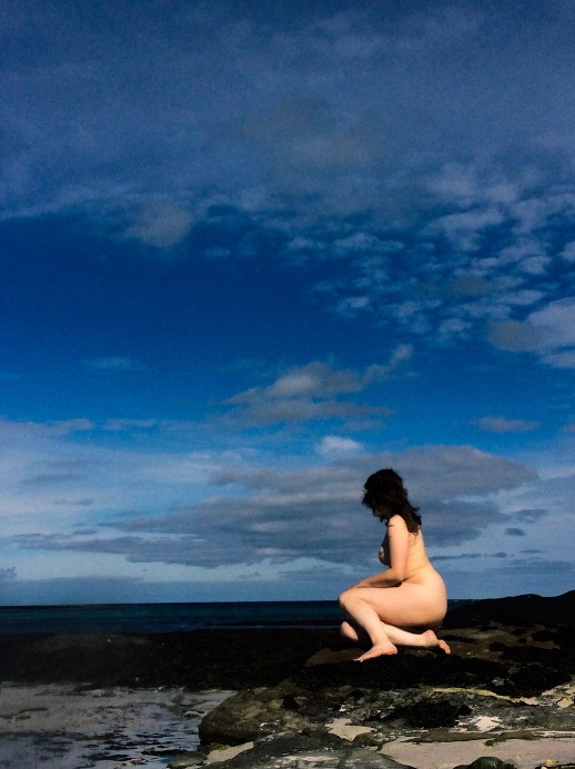 woman nude sitting on rocks looking out to sea