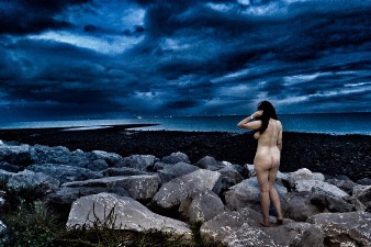 woman standing naked on rocks at the shore at nightfall
