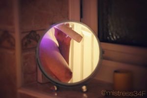 Reflection of topless woman holding toothbrush in small circular mirror