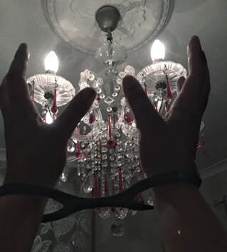 hands in wrist cuffs being held up in front of glass light fixture