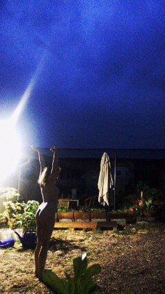 Nude woman reaching up into the rainy night sky