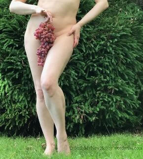 Woman holding large bunch of grapes in front of her vulva