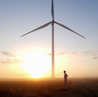 Nude man standing in front of wind turbine with sunrise