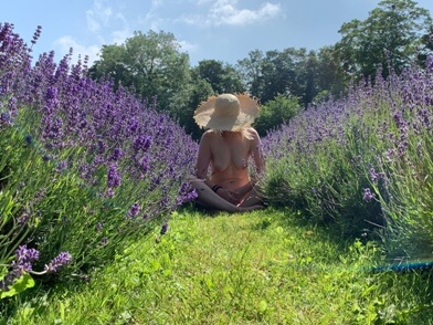 Woman sitting naked in sun hate in field of lavander