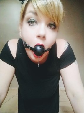 Woman looking into acamera wearing ball gag and droplet of spit haning from it