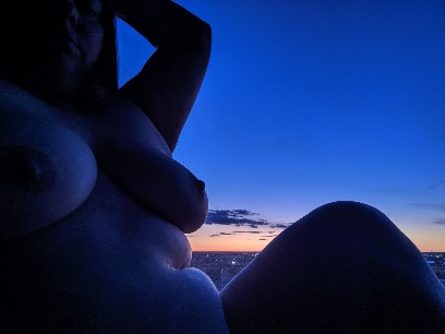 nude woman sitting by window with sunrise in the sky behind her