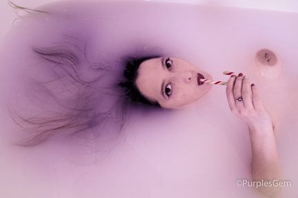 Woman laying in pink milk bath sucking on candy cane