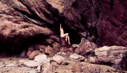 Woman sitting nude in a cave on the beach