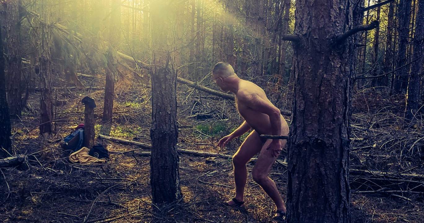Cropped image of naked man in woods with sunburst