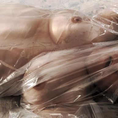 topless woman under plastic sheeting looking like doll