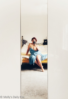 Molly in a blue towel with one breast showing sitting on the edge of her bed