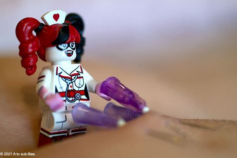 Harley Quinn Lego figure holding needles that are poking into Bee's skin