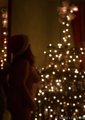 Molly standing naked in front of Christmas tree wearing santa hat
