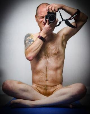Reflection of Man sitting naked crossed legged holding camera up to his face
