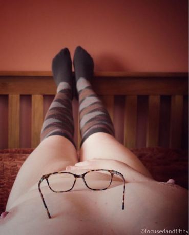 Missy laying with glasses on her chest looking down her naked body to her socks