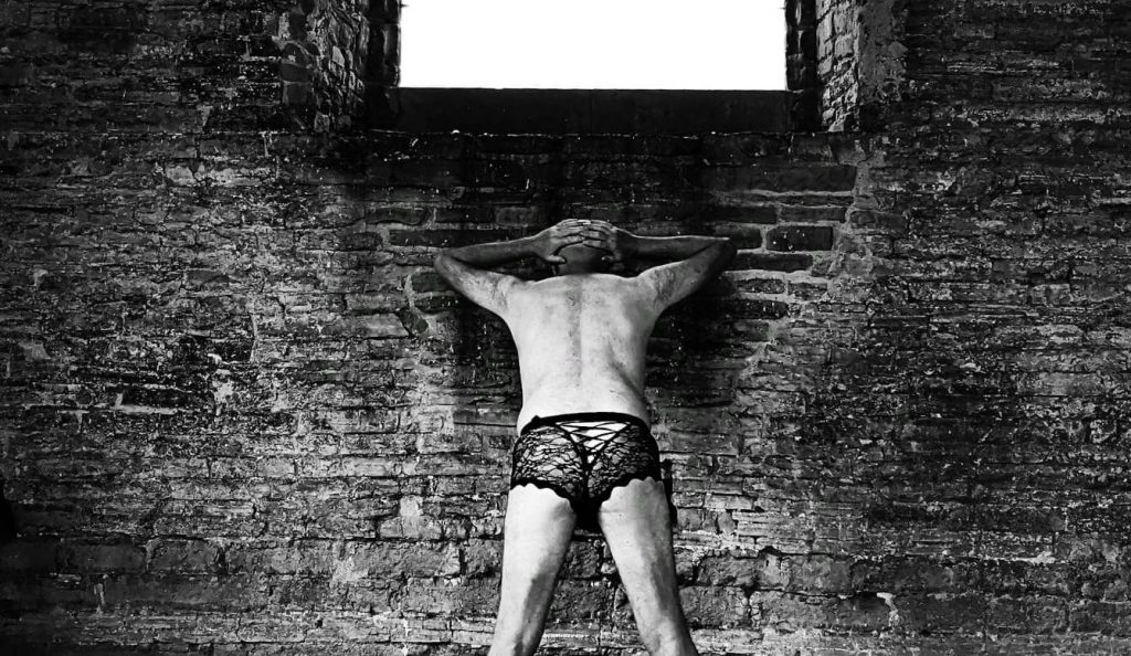 Cropped image of man in knickers up against wall of ruined church