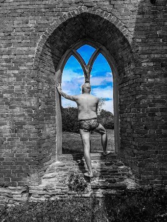 Man in lacy panties standing in front of window of ruined church