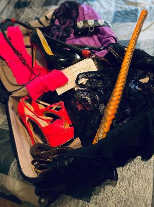 suitcase open showing contents of high heels, lacy knickers and spanking toys