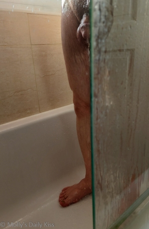 Man standing in the shower with water running down his penis and shower glass hiding half his body