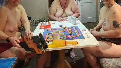 three topless people with breasts out playing a board game with spanking paddles on the table too
