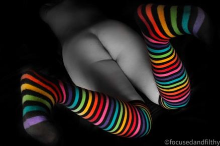 Looking down at Missy laying naked on her front with her feet kicked up wearing bright stripy knee high socks
