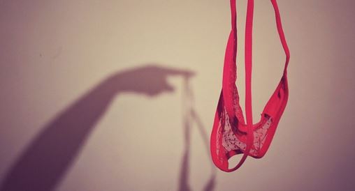 Shadow hand holding up red lace thong