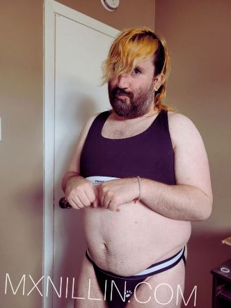 Nillin in jockstrap type pants a crop top looking at the camera with a coy shy expression