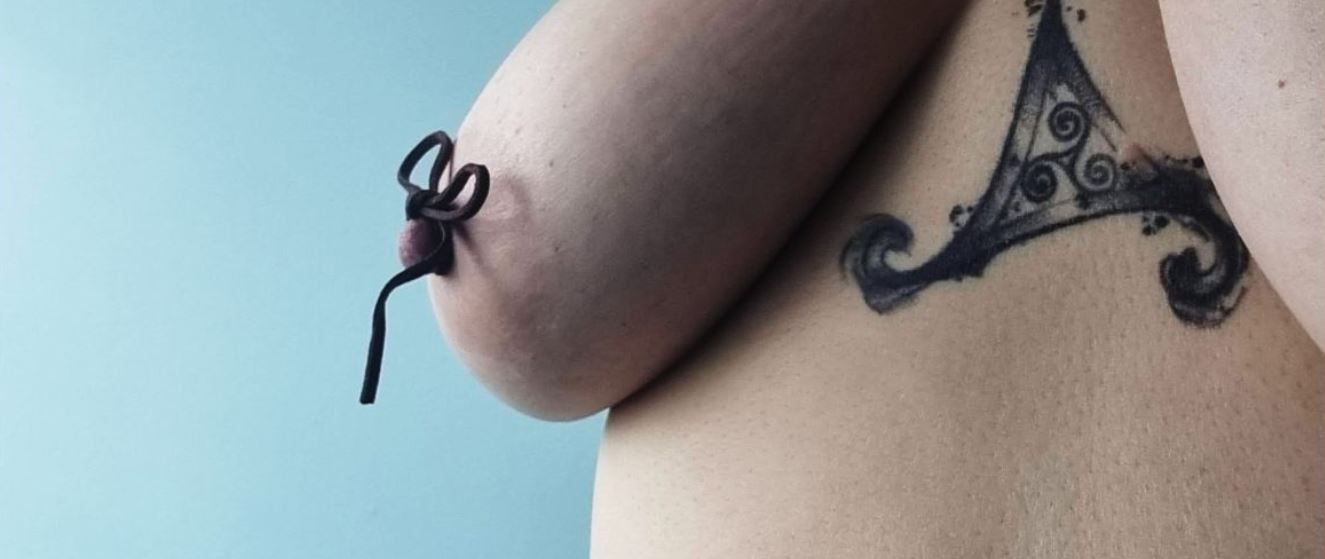 Honey's breast with leather tie on her nipple showing the tattoo between her breasts
