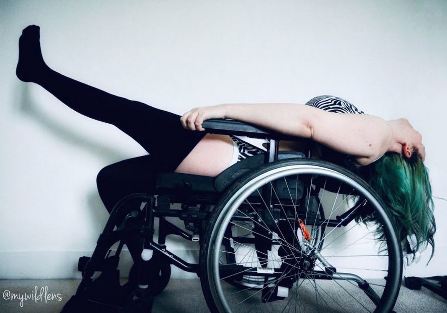 Image of Wild Lens in a wheel chair with her head thrown back and one leg up in the air