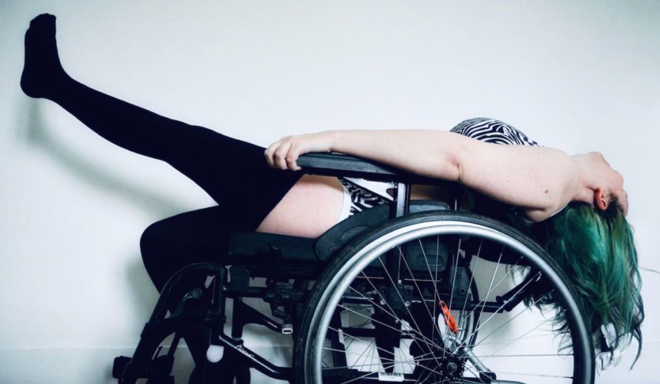 Cropped image of Wild Lens in a wheel chair with her head thrown back and one leg up in the air