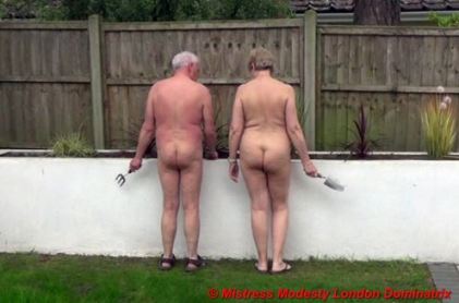 Naked couple with back to the camera holding gardening tools and looking down at the flower bed