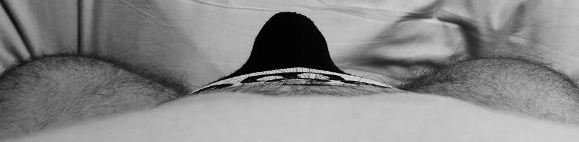 Black and white looking down mans body to black bulge in his pants