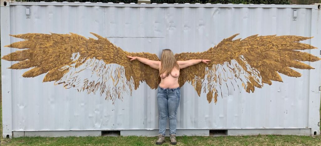 Mrs Jones standing topless in front of Angel wings wall art for weekly round-up 640