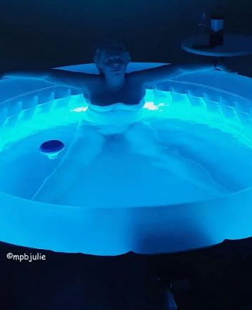Master's Pleasing Bitch in blue water of hot tub with dark all around