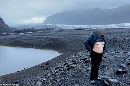 Bee standing next to water in barren Iceland landscape with their top pulled up to show their breasts