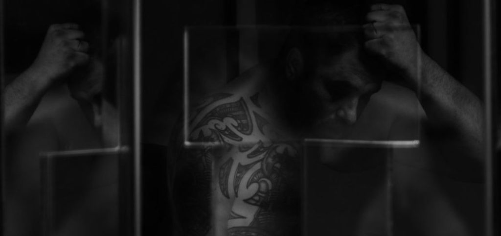 Black and white multiple exposure of man caught in the mirror through a key hole. We can see his biceps and forearms which are laced with tattoos for post called mirror mirror