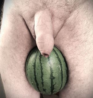 Man standing with watermelon between his thighs and his penis hanging down in front of it for weekly round-up 696